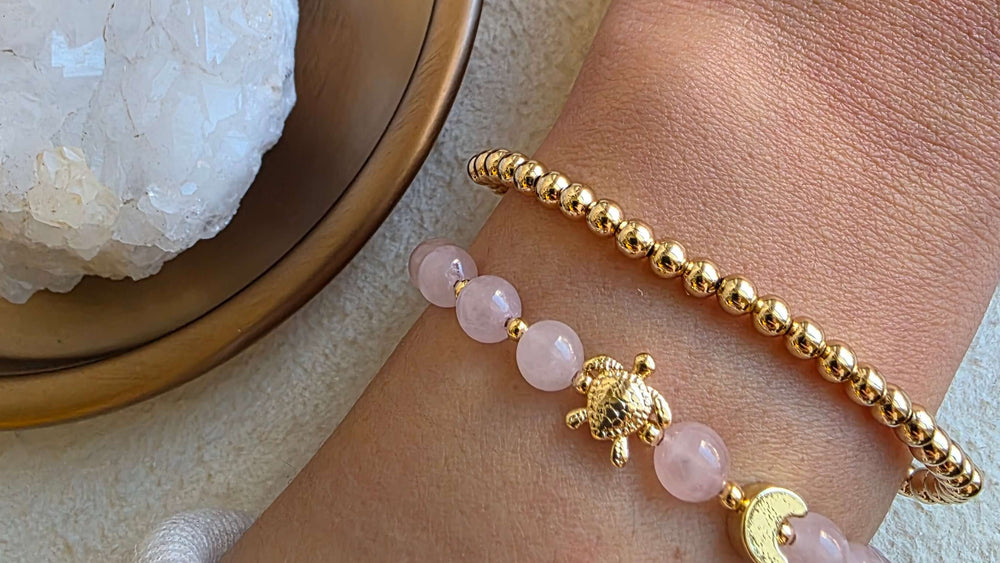 Gold and pink beaded bracelet on a wrist with a crystal dish in the background
