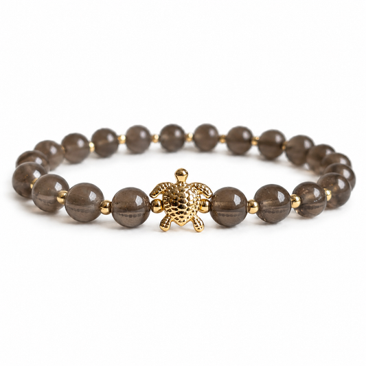 Bracelet with smoky quartz stone beads and a gold turtle charm on a white background