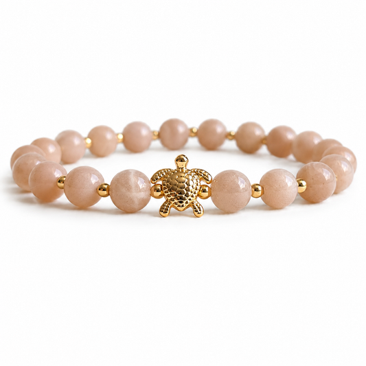 Bracelet with coral peach beads and a gold turtle charm on a white background