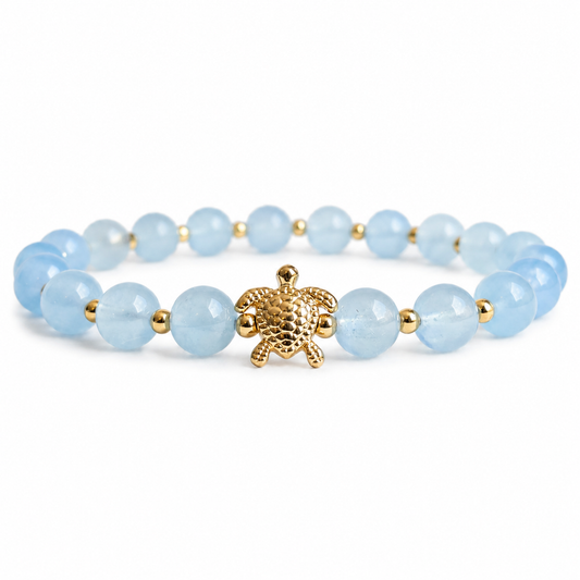 Bracelet with light blue aquamarine stone beads and a gold turtle charm on a white background